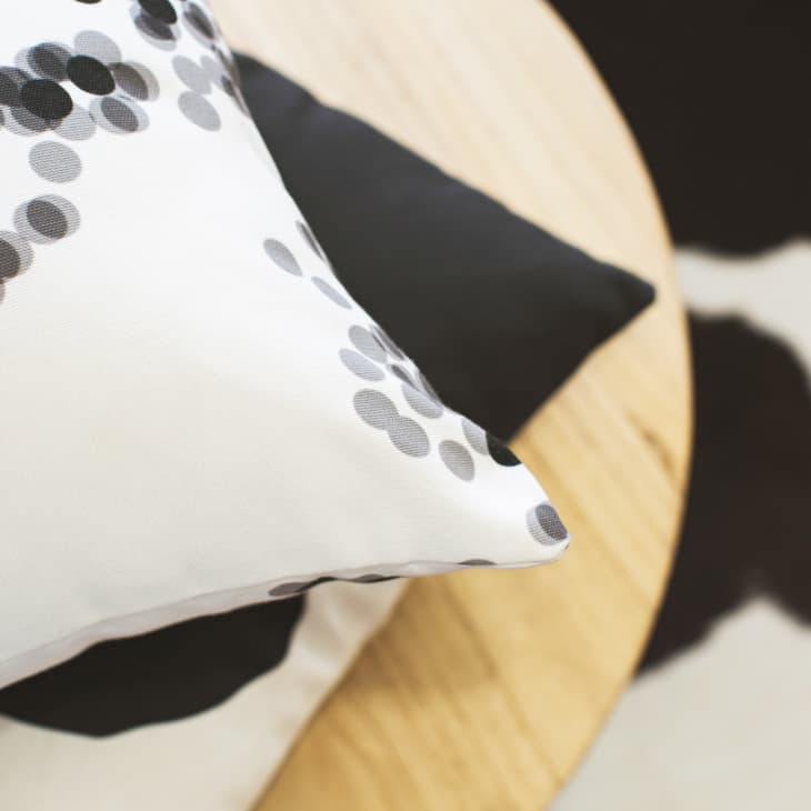 Polka dot pillow on a wooden table with a black and white patterned rug.