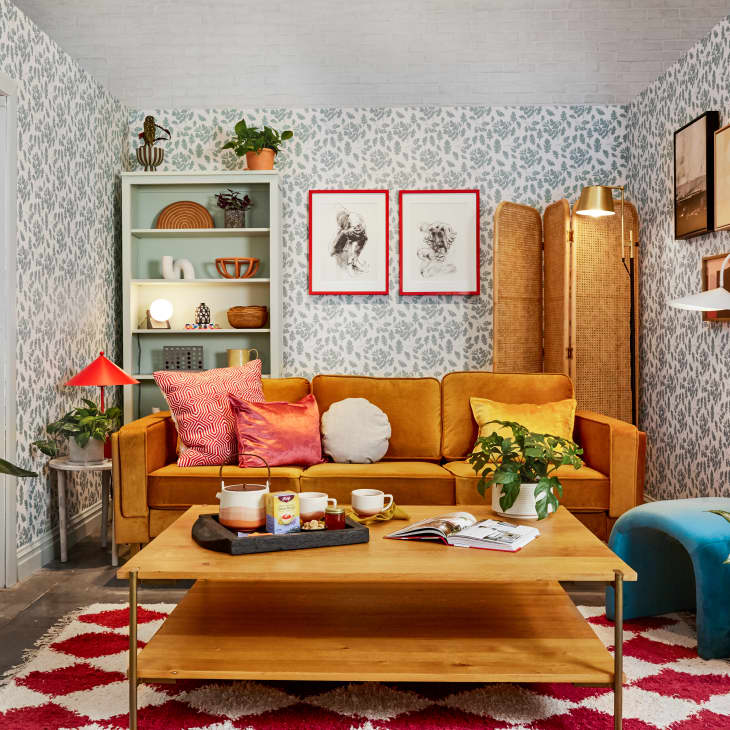 bright happy living space with gold velvet sofa, coffee table with yogi tea setup, patterned wallpaper, red and white rug, shelves with l'objets, plants