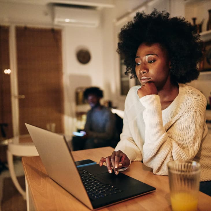 Beautiful African American woman studying in the living room on a laptop computer while living with her boyfriend.