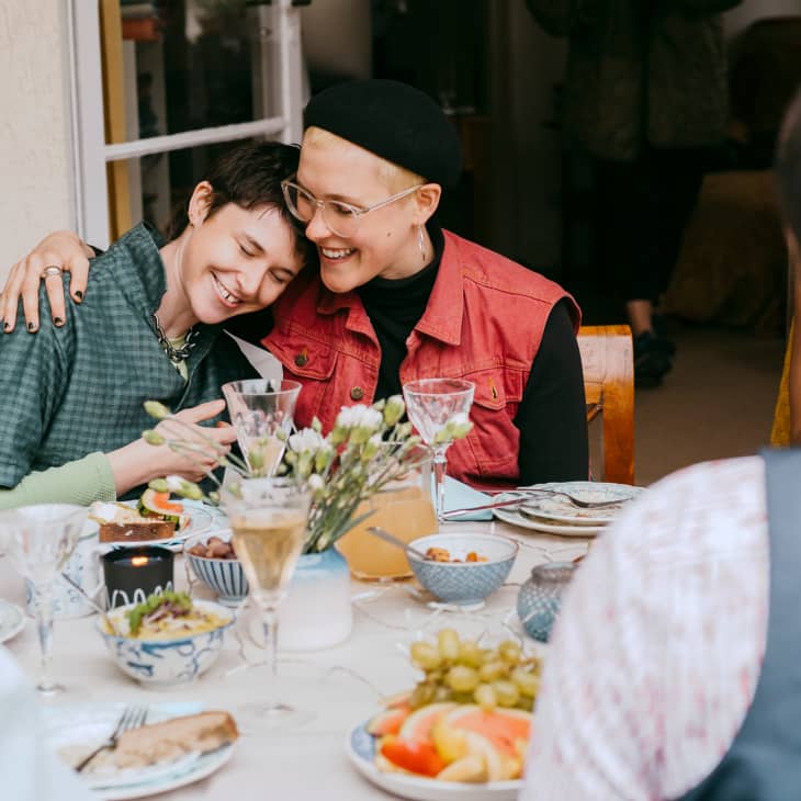 Smiling gay woman sitting with arm around non-binary friend during party in back yard