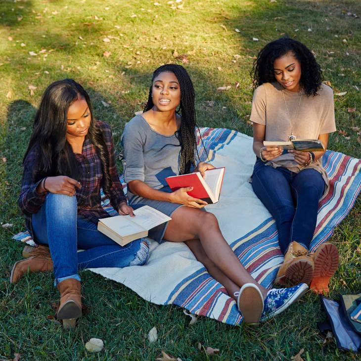 Three friends reading books on a blanket in a park in early Fall