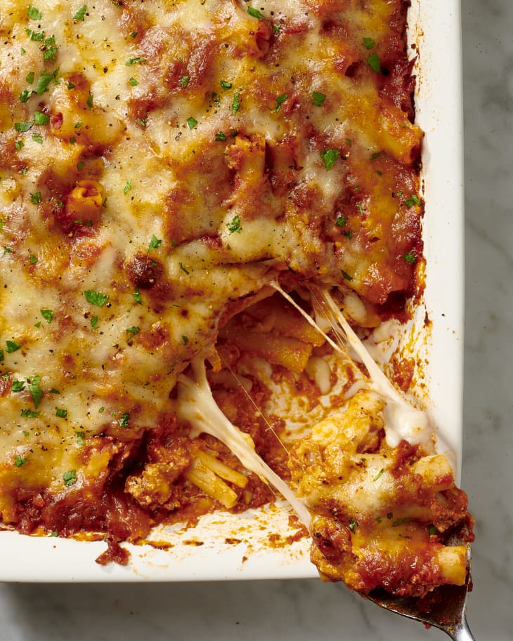 photo of baked ziti in a white casserole dish with a serving being pulled away showing a cheese pull