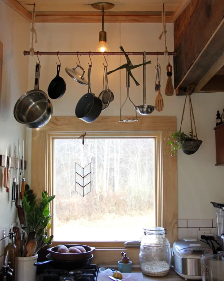 Small kitchen with hanging pots, wooden counter, gas stove, and large window overlooking a wooded area.