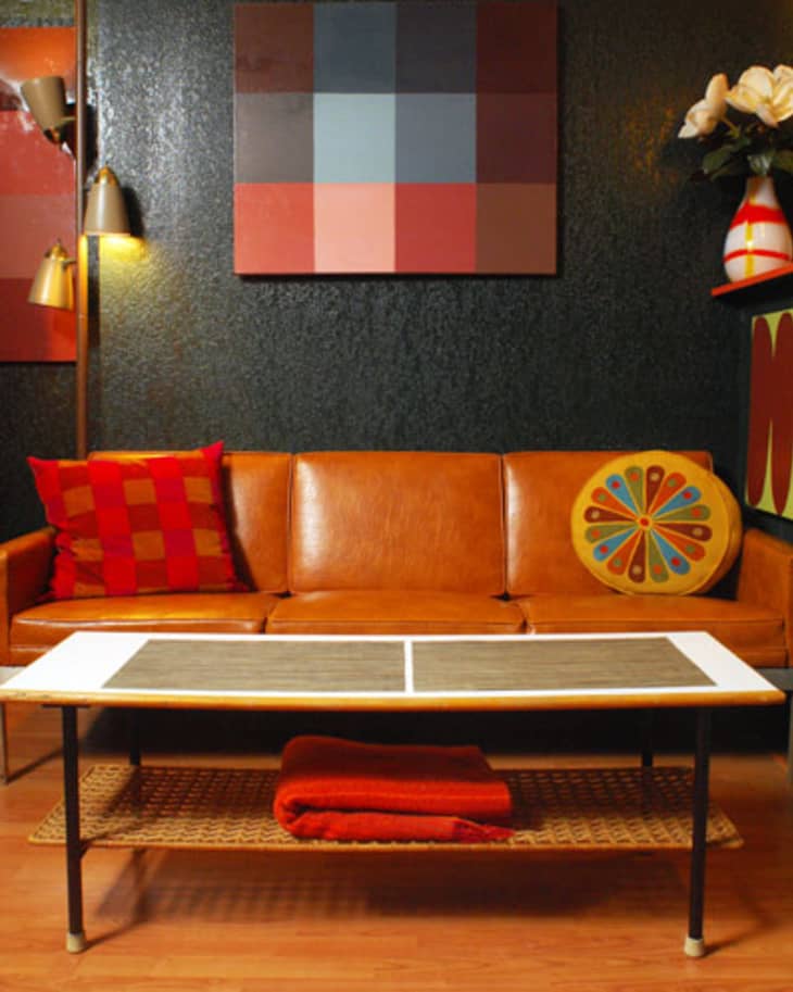 Mid-century modern living room with a brown leather sofa, colorful pillows, geometric wall art, and a wicker coffee table.
