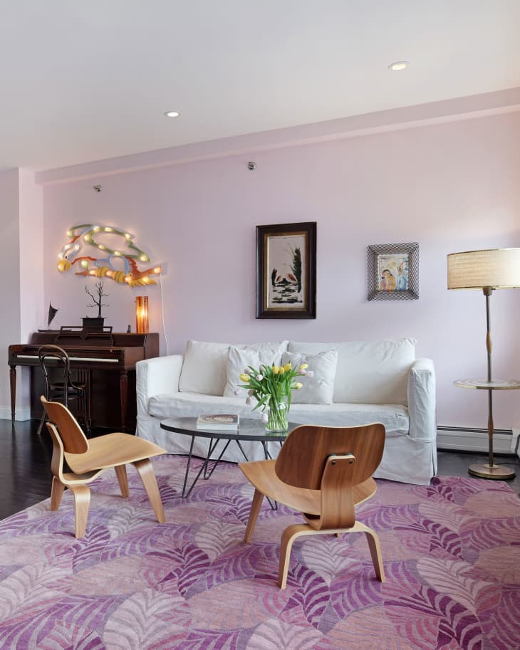 Living room with white sofa, wooden chairs, glass coffee table, piano, and purple leaf-patterned rug.