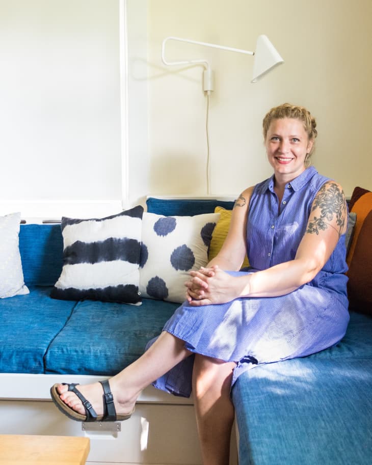 Woman in a blue dress sitting on a blue sofa with patterned cushions, under a white wall lamp.