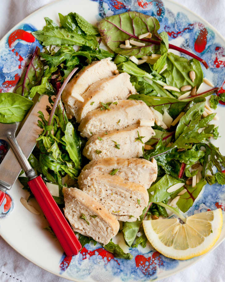 Slices of moist and tender chicken breast, served with simple salad and garnished with lemon wedge, on a plate