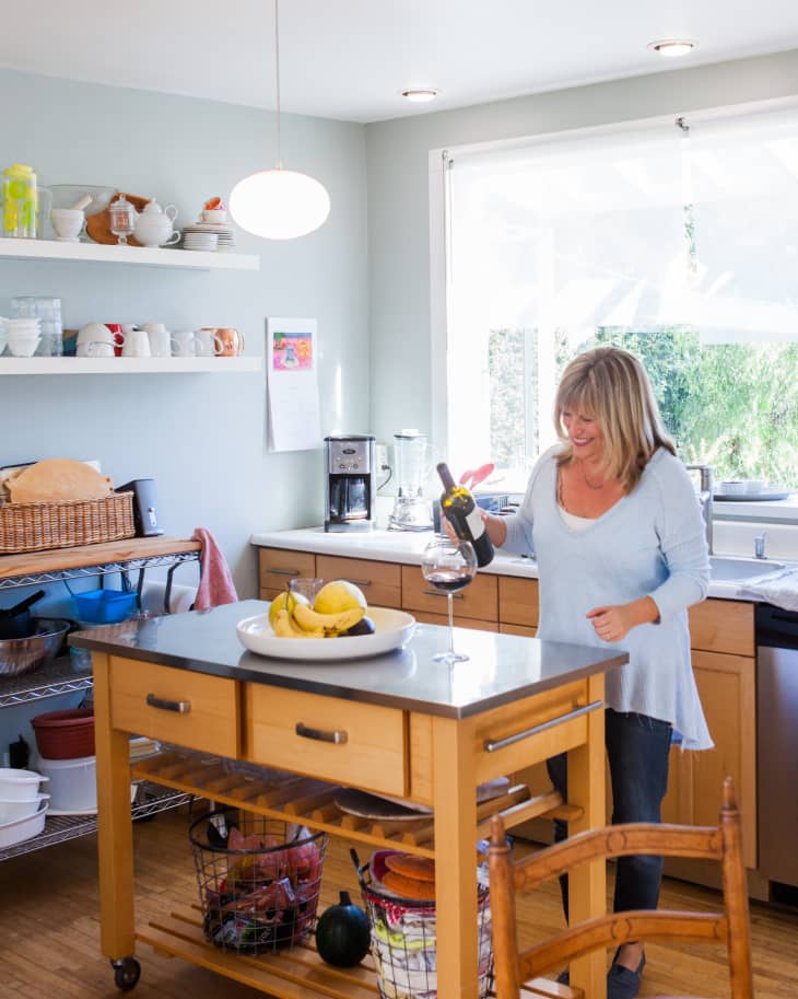 Woman holding wine bottle in kitchen over a kitchen island cart