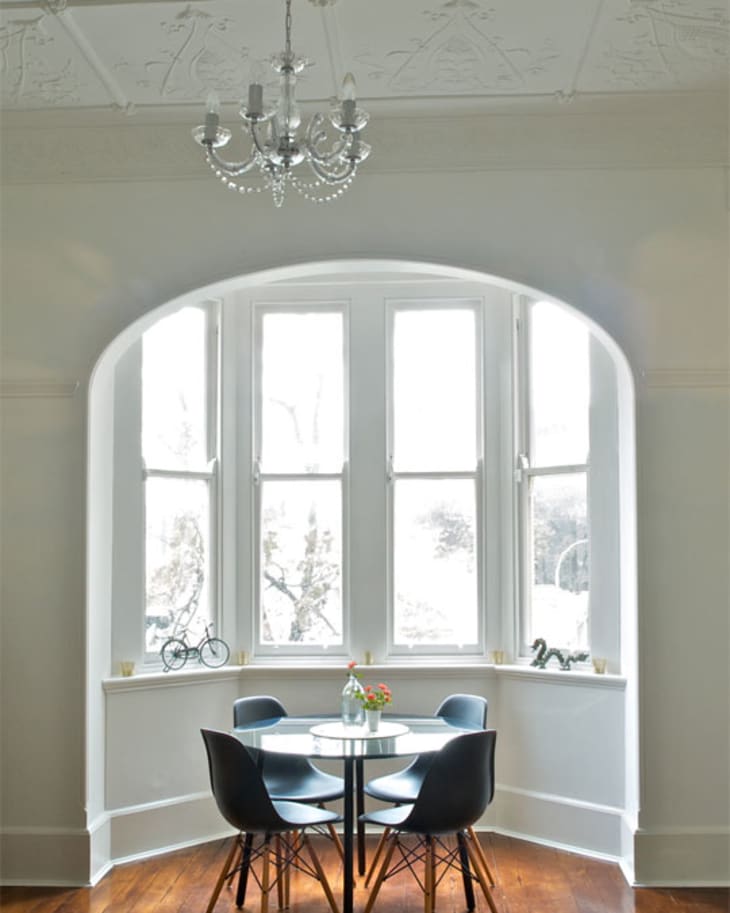 Dining area with round table, four black chairs, large bay windows, and a chandelier.