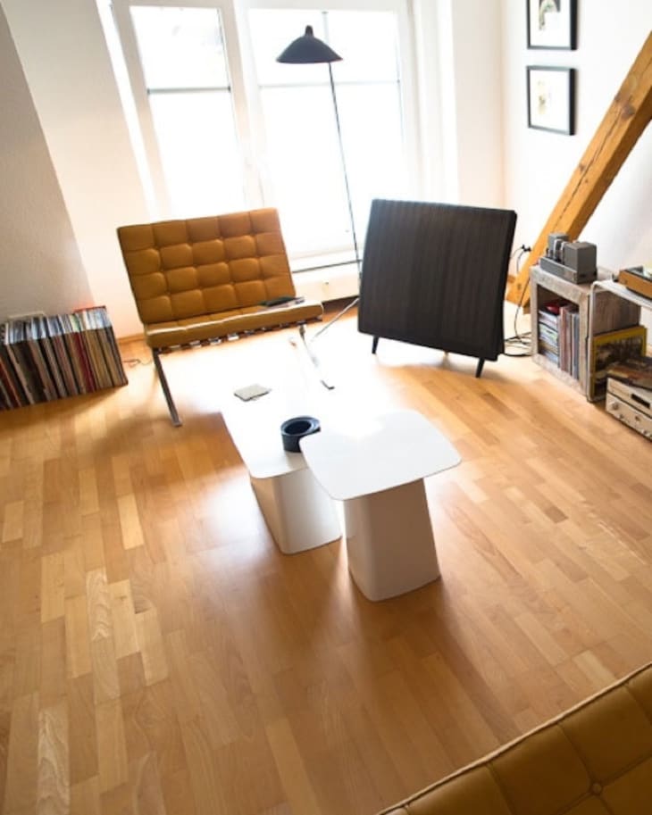 Mid-century modern living room with mustard chair, black lamp, white coffee table, and vinyl records on wooden floor.