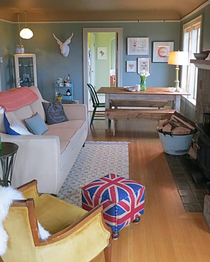 Cozy living room with beige sofa, Union Jack ottoman, yellow chair, and wooden dining table near a fireplace.