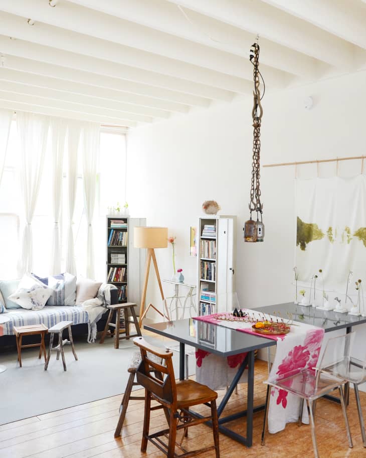 Bright living room with a glass dining table, wooden chairs, bookshelves, and a cozy sofa with striped cushions.