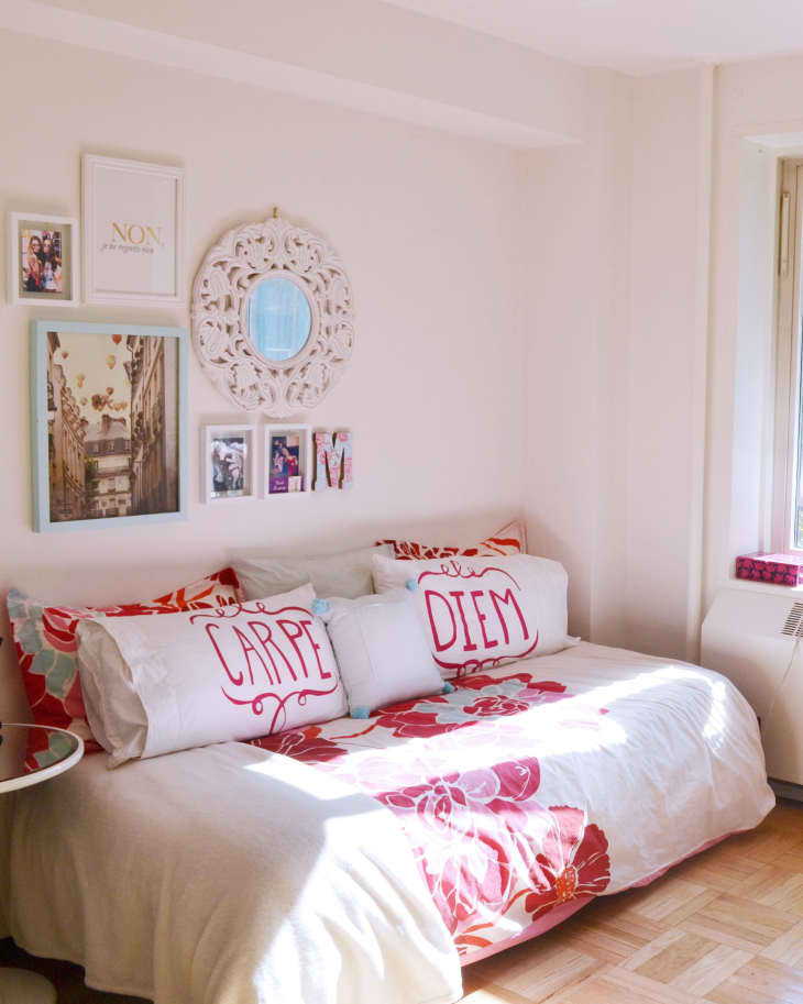Bedroom with floral bedding, "Carpe Diem" pillows, wall art, and a small side table with a black bag.