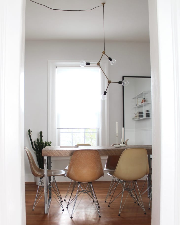 Dining room with wooden table, six brown chairs, modern chandelier, and a cactus by the window.