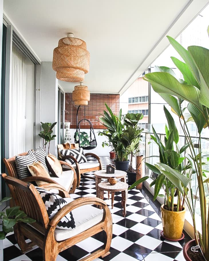 Balcony with wooden chairs, black and white checkered floor, potted plants, and wicker pendant lights.