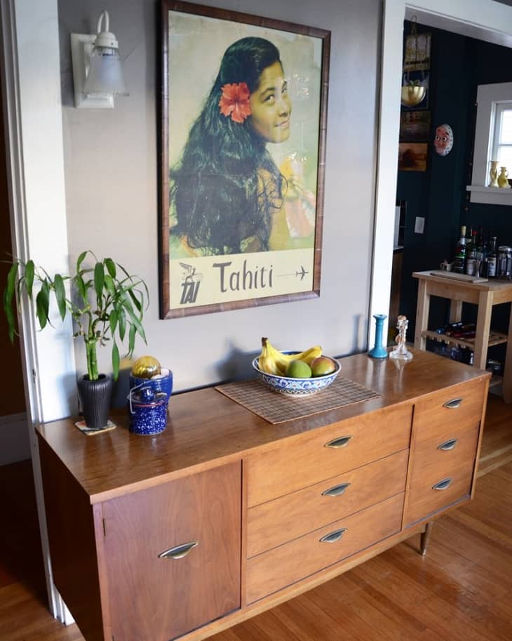 Mid-century modern sideboard with a Tahiti poster above, a potted plant, and a fruit bowl on top.