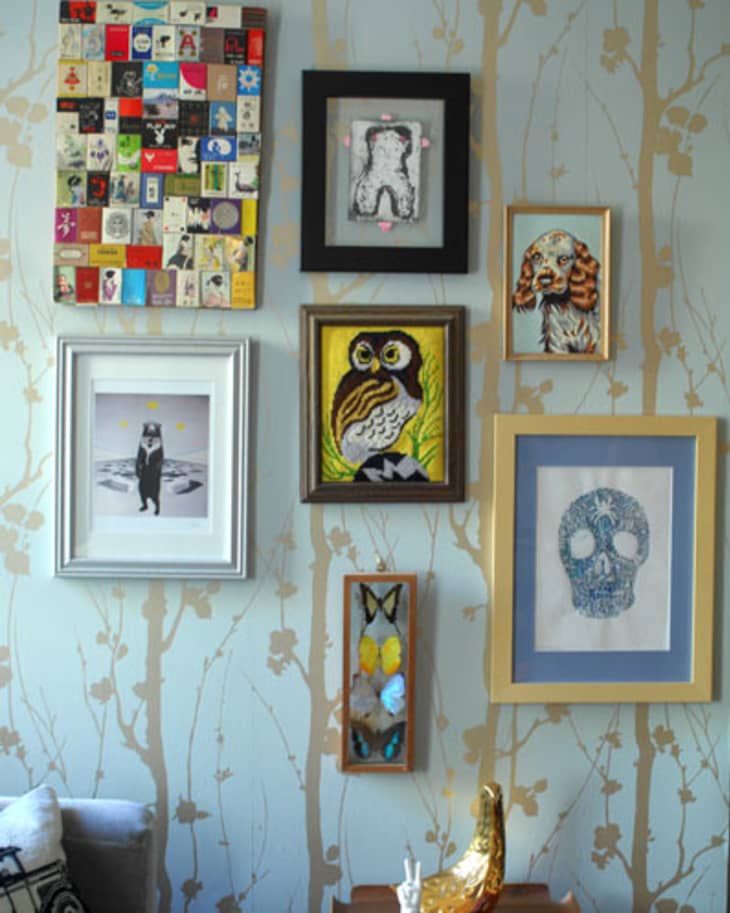 Gallery wall with eclectic framed art, including an owl, skull, and abstract designs, on patterned wallpaper.