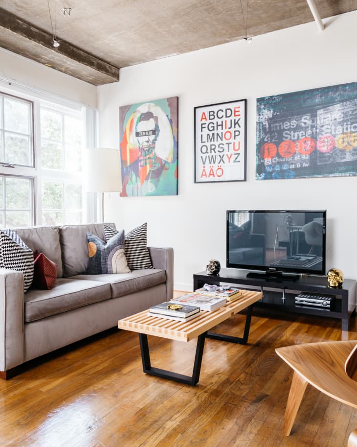 Modern living room with gray sofa, colorful pillows, wooden coffee table, TV, and abstract wall art.