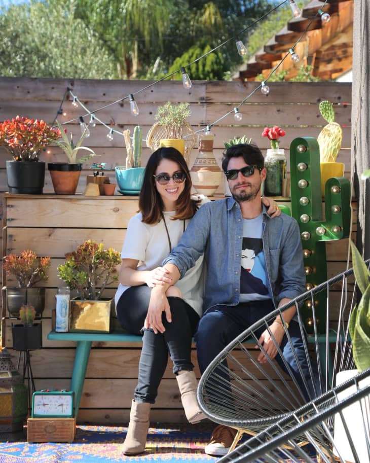 Couple sitting on a patio bench surrounded by potted succulents and cacti, with string lights overhead.
