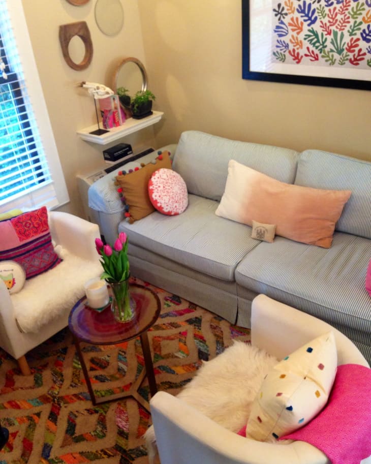 Cozy living room with a striped sofa, colorful cushions, patterned rug, and tulips on a round wooden table.