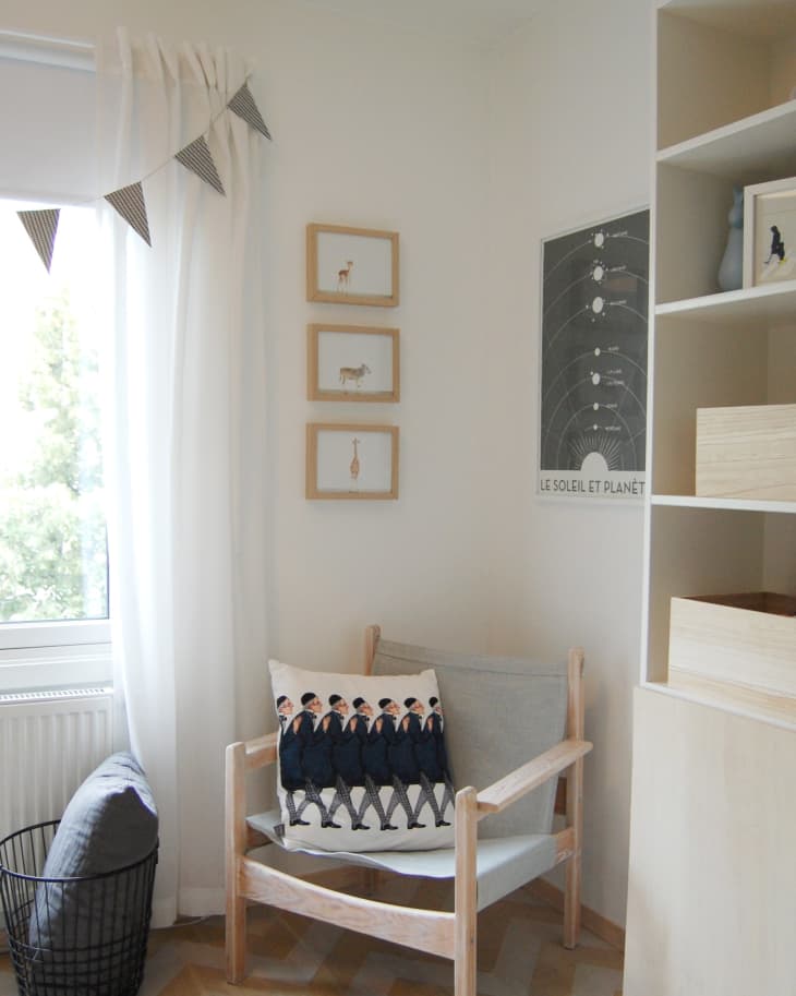 Cozy corner with a wooden chair, graphic pillow, framed animal art, and a solar system poster.