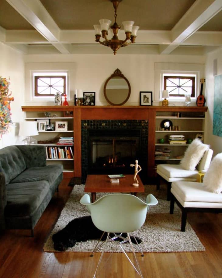 Cozy living room with a fireplace, green sofa, white chairs, and a light blue chair on a rug.