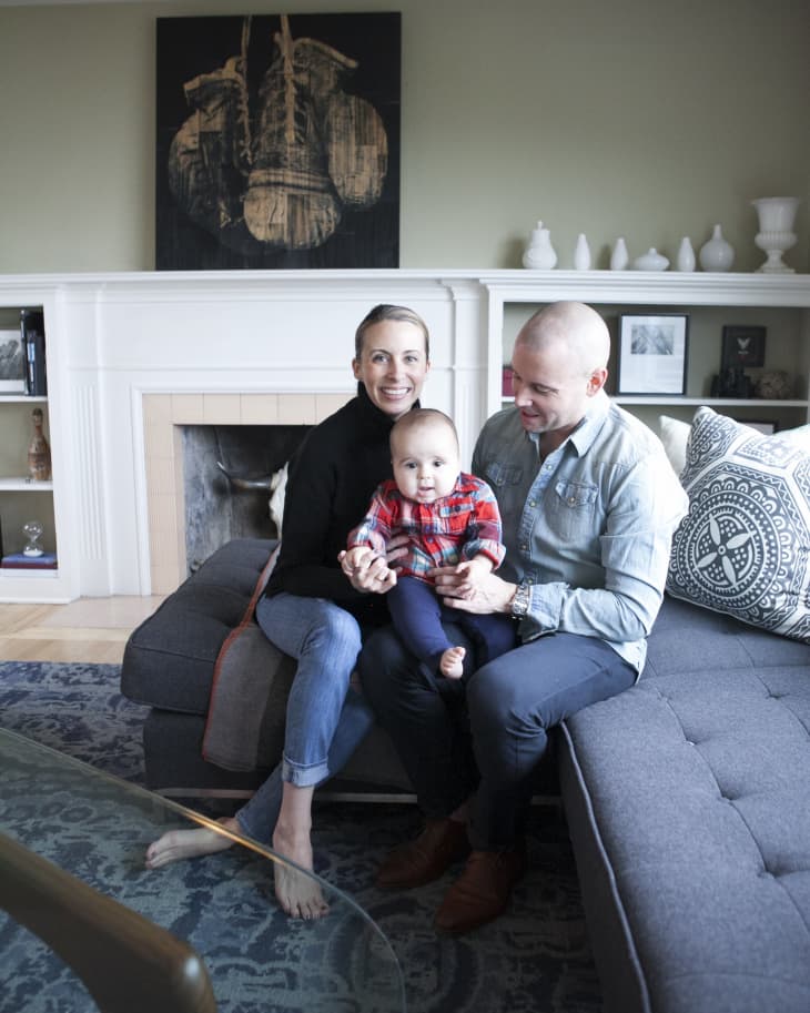 Family sitting on a gray sectional sofa in a living room with a fireplace and abstract wall art.