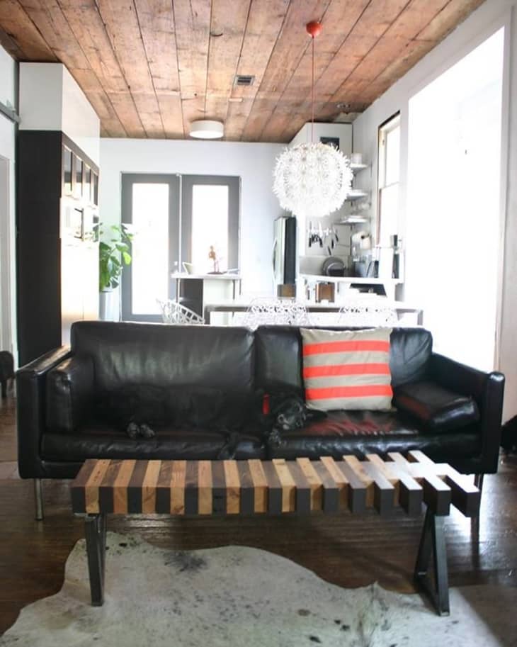 Black leather sofa with striped pillow, wooden coffee table, cowhide rug, and modern pendant light in a rustic living room.