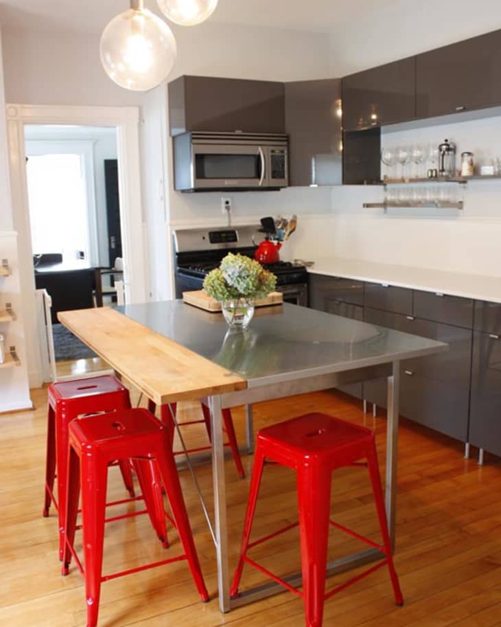Modern kitchen with gray cabinets, red stools, metal island, wooden countertop, and pendant lights.