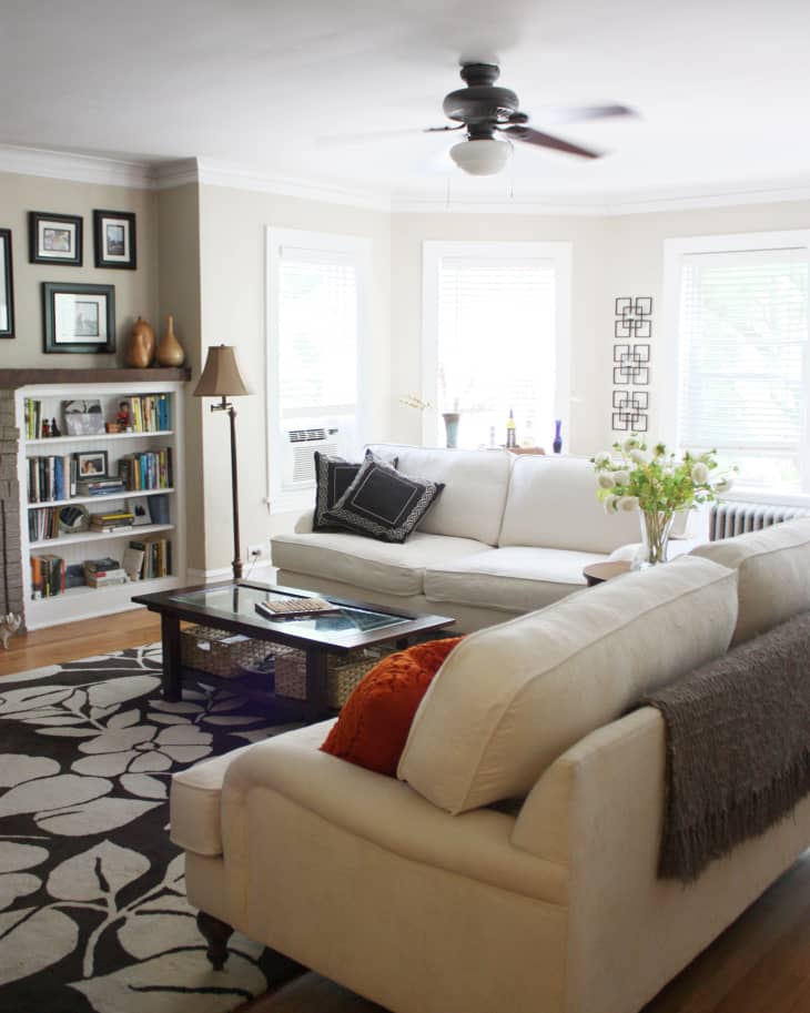 Living room with cream sofas, black and white floral rug, bookshelf, and ceiling fan.