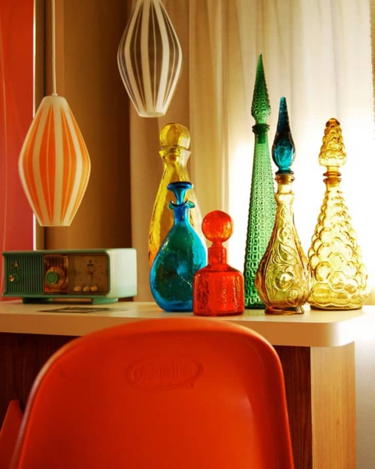 Colorful glass decanters on a table with a retro radio, orange chair, and pendant lights.