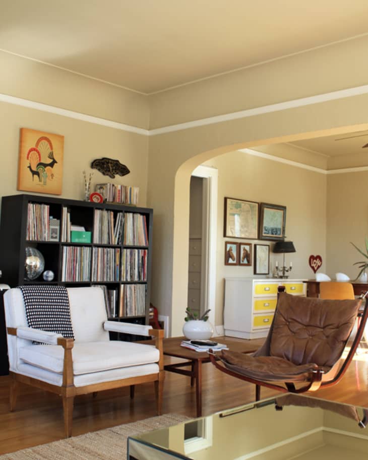 Living room with a white armchair, brown leather chair, black bookshelf filled with records, and a yellow dresser.