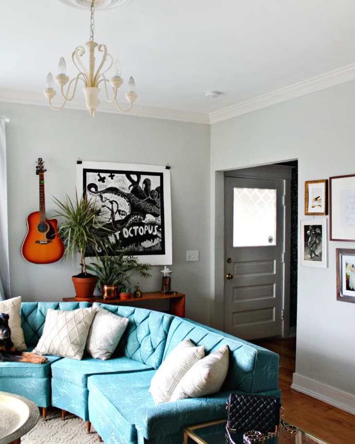 Living room with teal sectional sofa, guitar on wall, octopus artwork, potted plants, and chandelier.