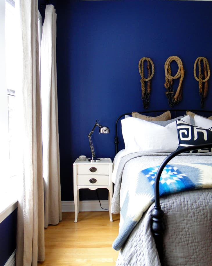 Bedroom with blue walls, white nightstand, metal lamp, and rope decor above bed.