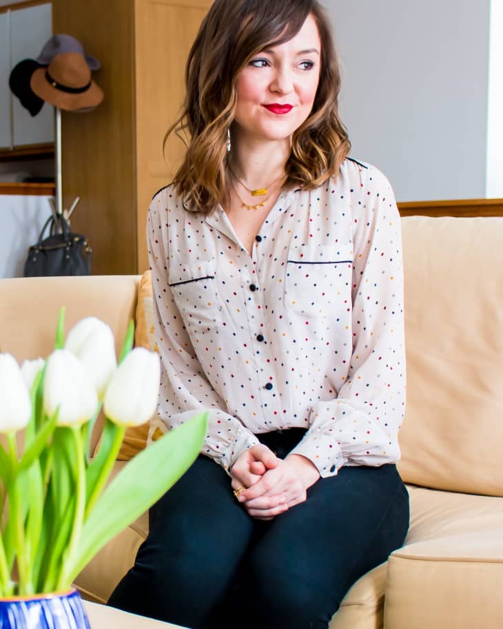 Woman in polka dot blouse sitting on beige sofa, with white tulips in foreground.