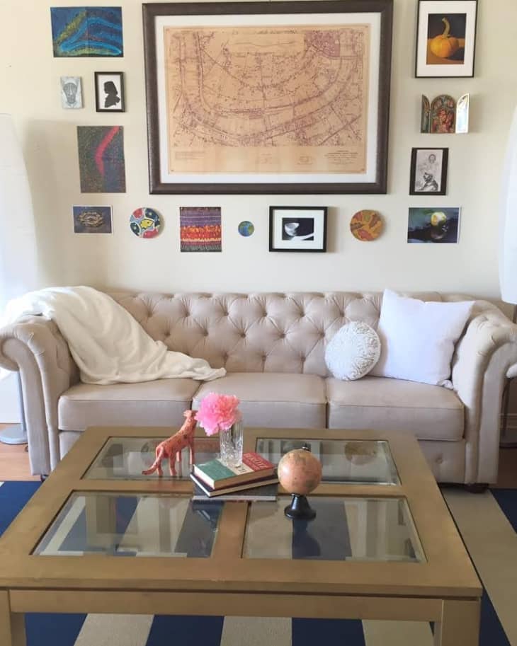 Beige tufted sofa with white pillows, glass coffee table, pink flowers, and eclectic wall art in a cozy living room.