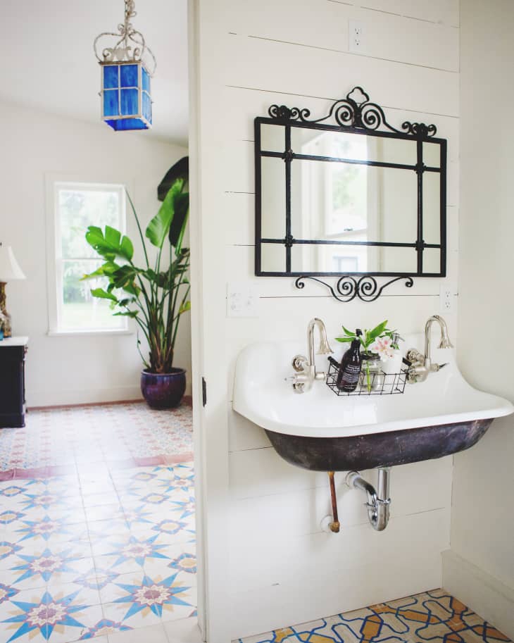 Bathroom with a vintage sink, ornate mirror, and patterned tile floor, adjacent to a room with a large potted plant.