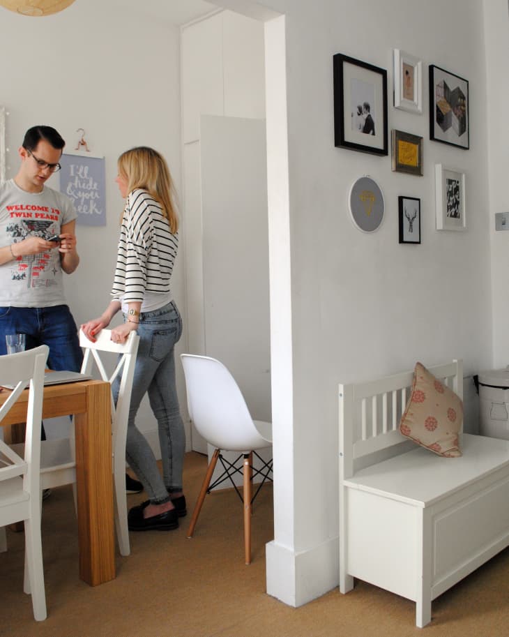 Couple standing in a dining area with a wooden table, white chairs, and a gallery wall.