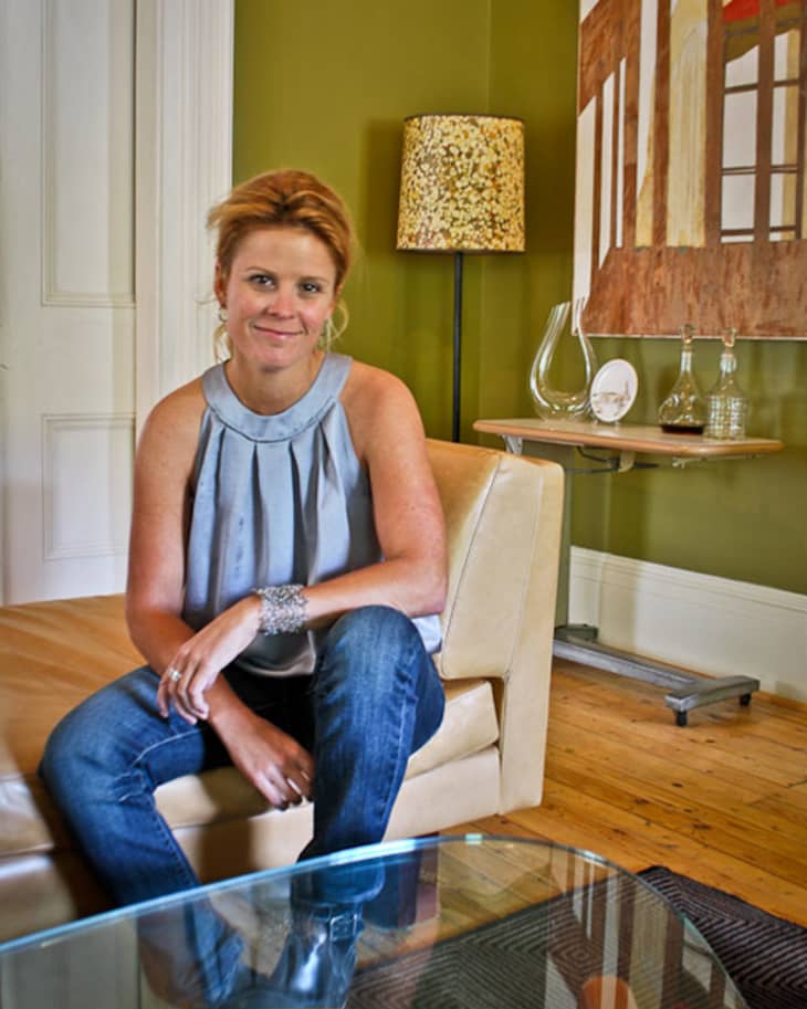 Woman sitting on a beige sofa in a living room with green walls, a patterned lamp, and abstract art.