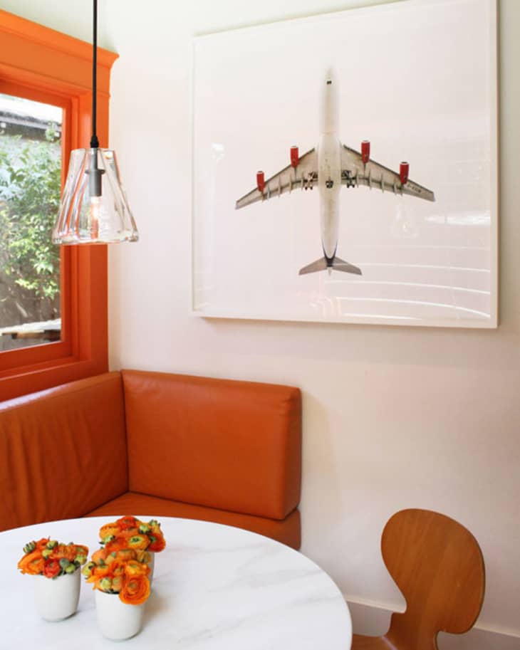 Cozy breakfast nook with orange banquette, round table, floral centerpiece, and airplane artwork.