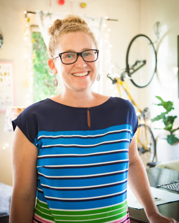 Person smiling in a room with a striped dress, glasses, and a bicycle on the wall.