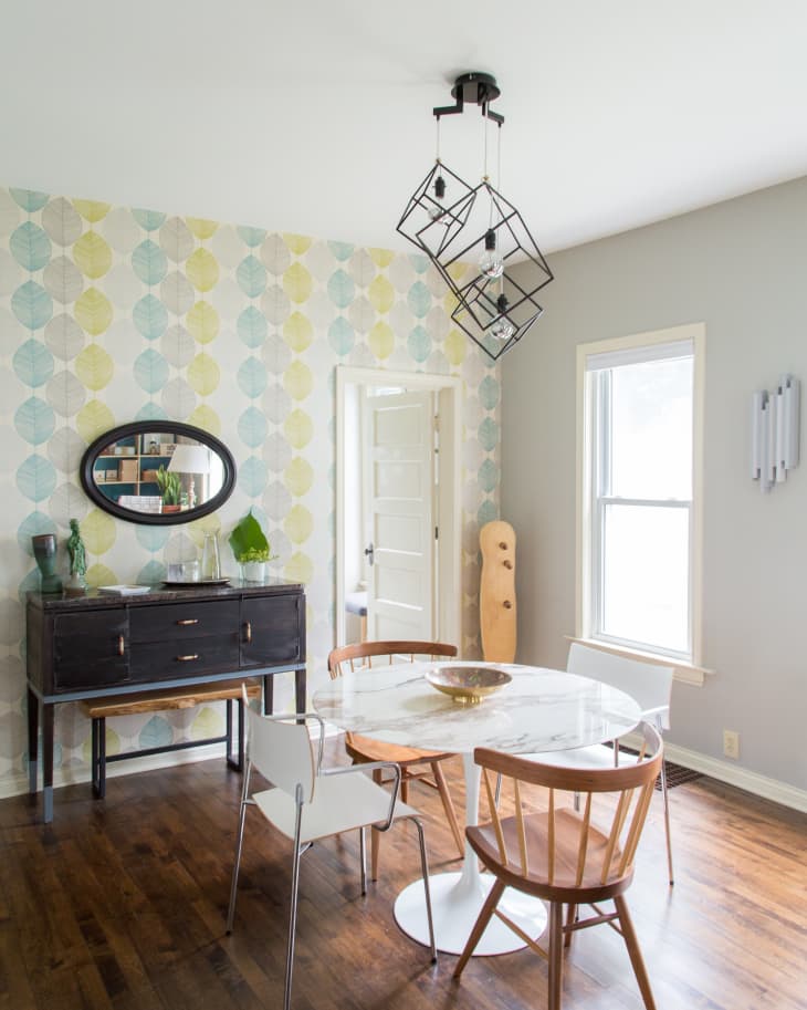 Dining room with a round marble table, mixed chairs, geometric light fixture, and patterned wallpaper.
