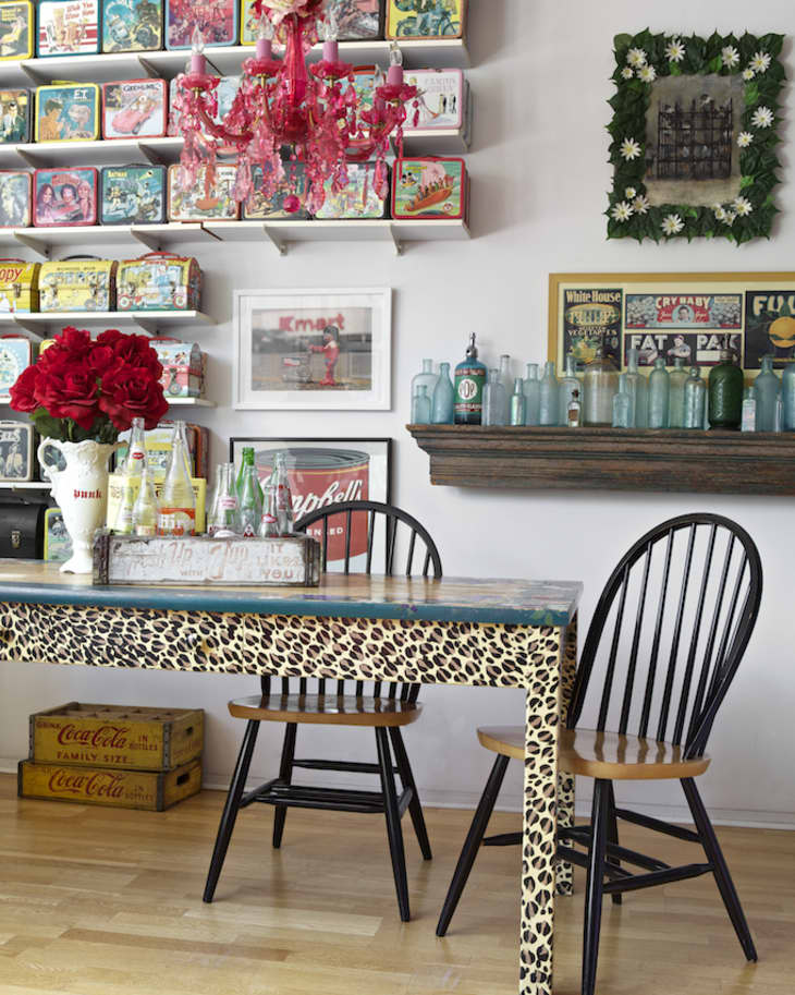 Eclectic dining area with leopard print table, red chandelier, vintage lunchboxes, and black chairs.