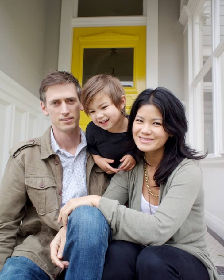 A family of three sitting on steps, with a yellow door in the background.