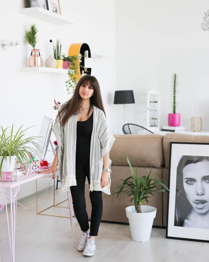 Woman in a modern living room with plants, framed art, and decorative shelves.