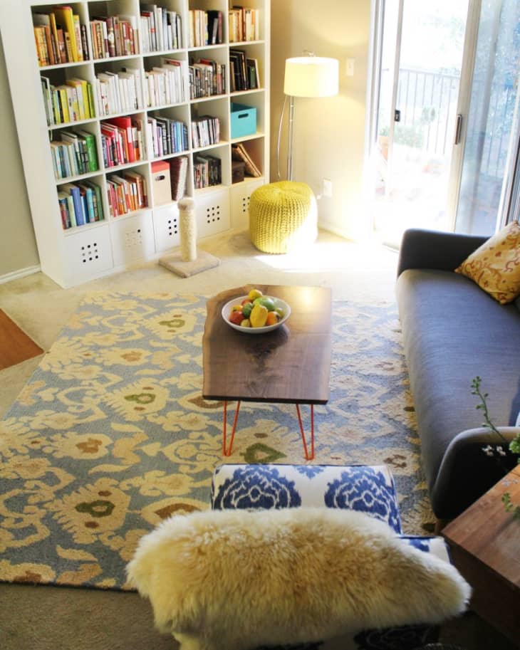 Living room with a large bookshelf, patterned rug, gray sofa, and wooden coffee table with a fruit bowl.