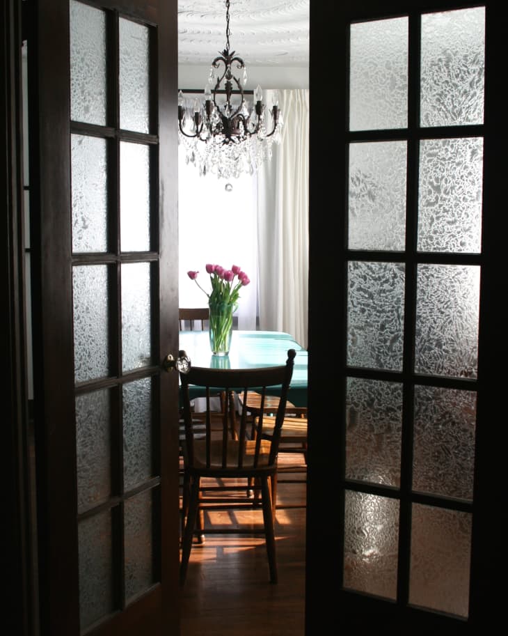 French doors opening to dining room with chandelier, wooden chairs, and a vase of pink tulips on the table.