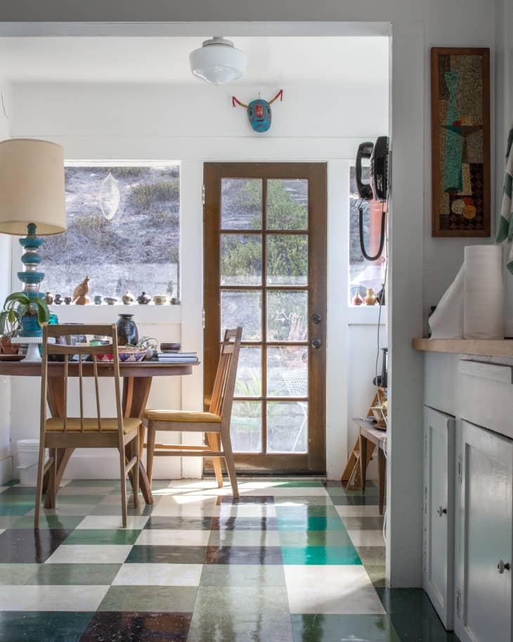 Dining area with wooden table and chairs, colorful checkered floor, and glass door leading outside.