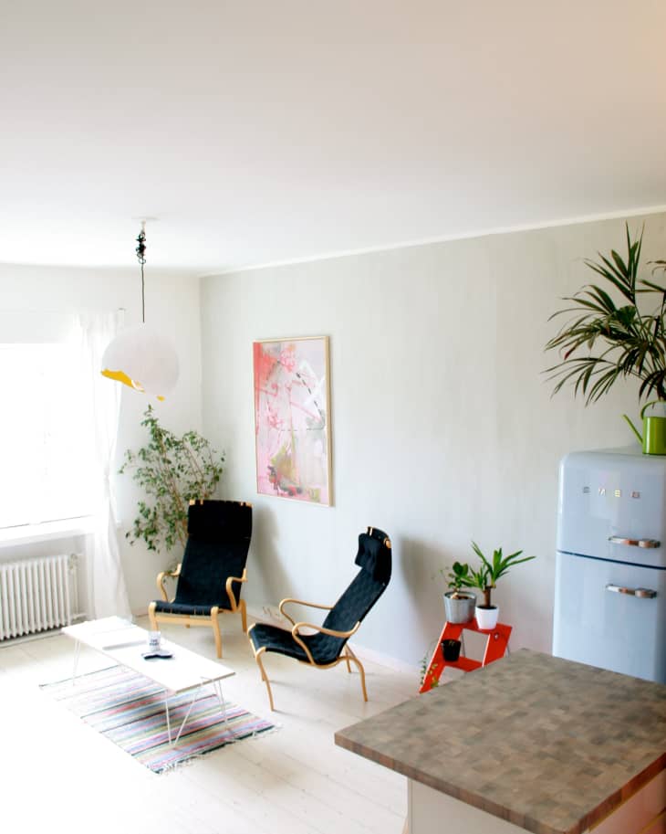 Bright living room with two black lounge chairs, a white coffee table, colorful rug, plants, and a retro-style fridge.