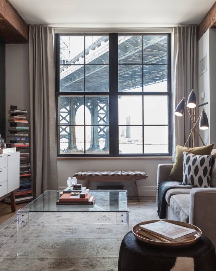 Living room with glass coffee table, gray sofa, patterned pillows, and large window view of a bridge.